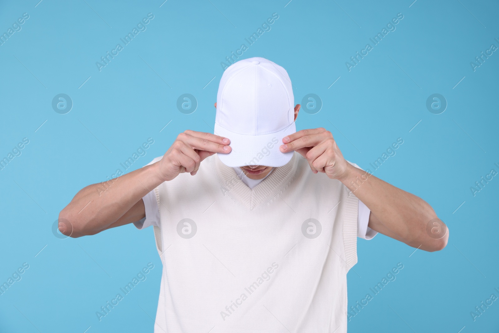 Young man wearing stylish white baseball hat on light blue background Photo of Young man wearing stylish white baseball hat on light blue background