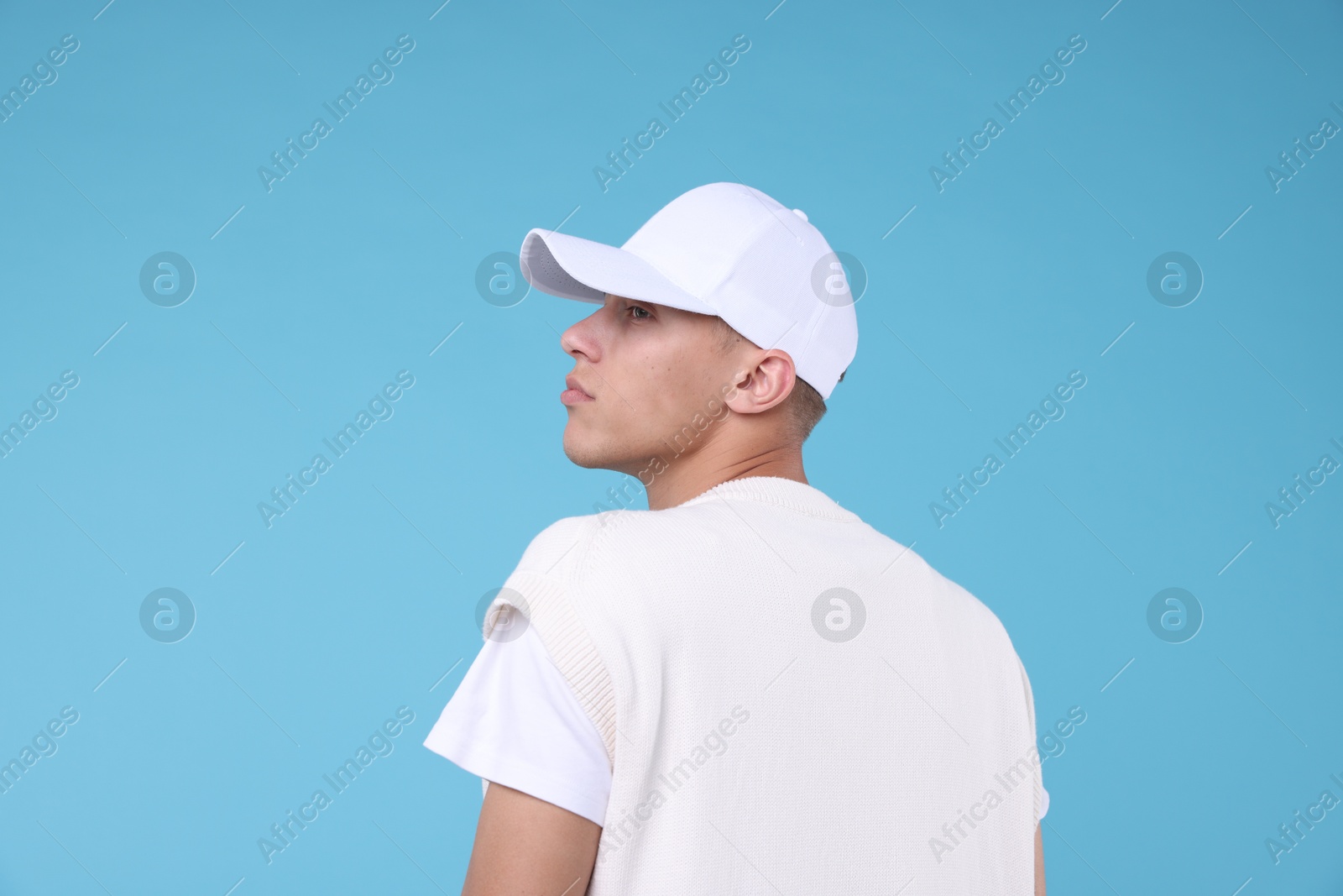 Young man wearing stylish white baseball hat on light blue background Photo of Young man wearing stylish white baseball hat on light blue background
