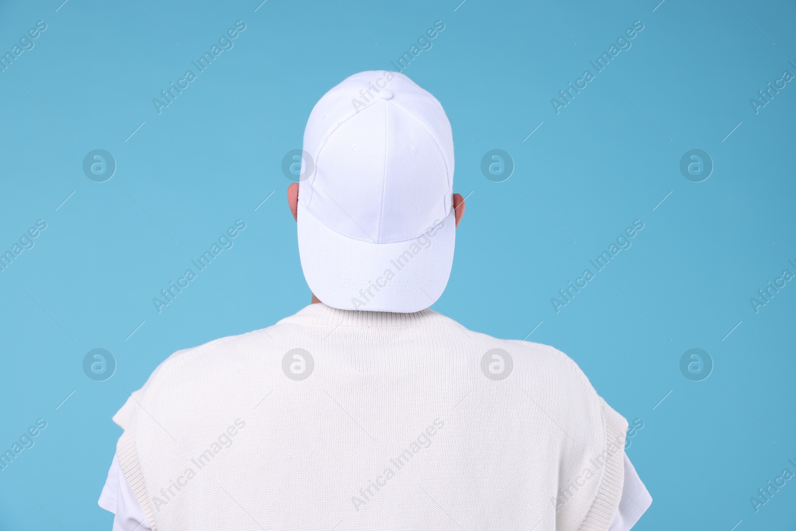Young man wearing stylish white baseball hat on light blue background, back view Photo of Young man wearing stylish white baseball hat on light blue background, back view
