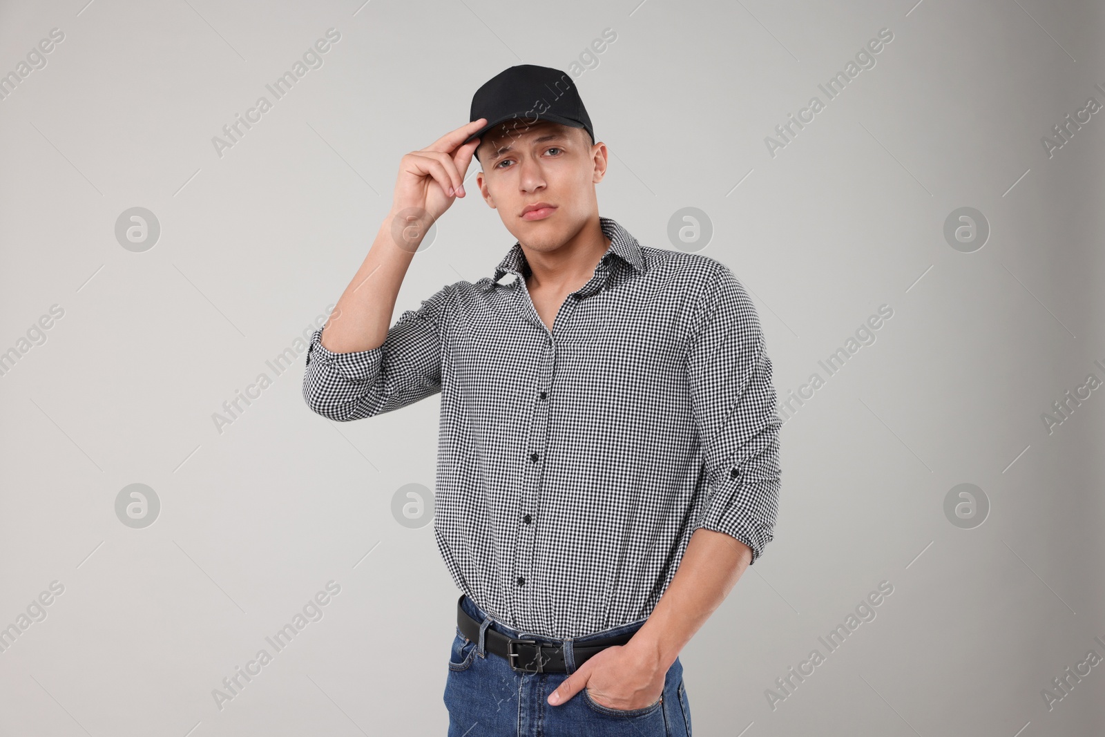 Young man wearing stylish black baseball hat on light grey background Photo of Young man wearing stylish black baseball hat on light grey background