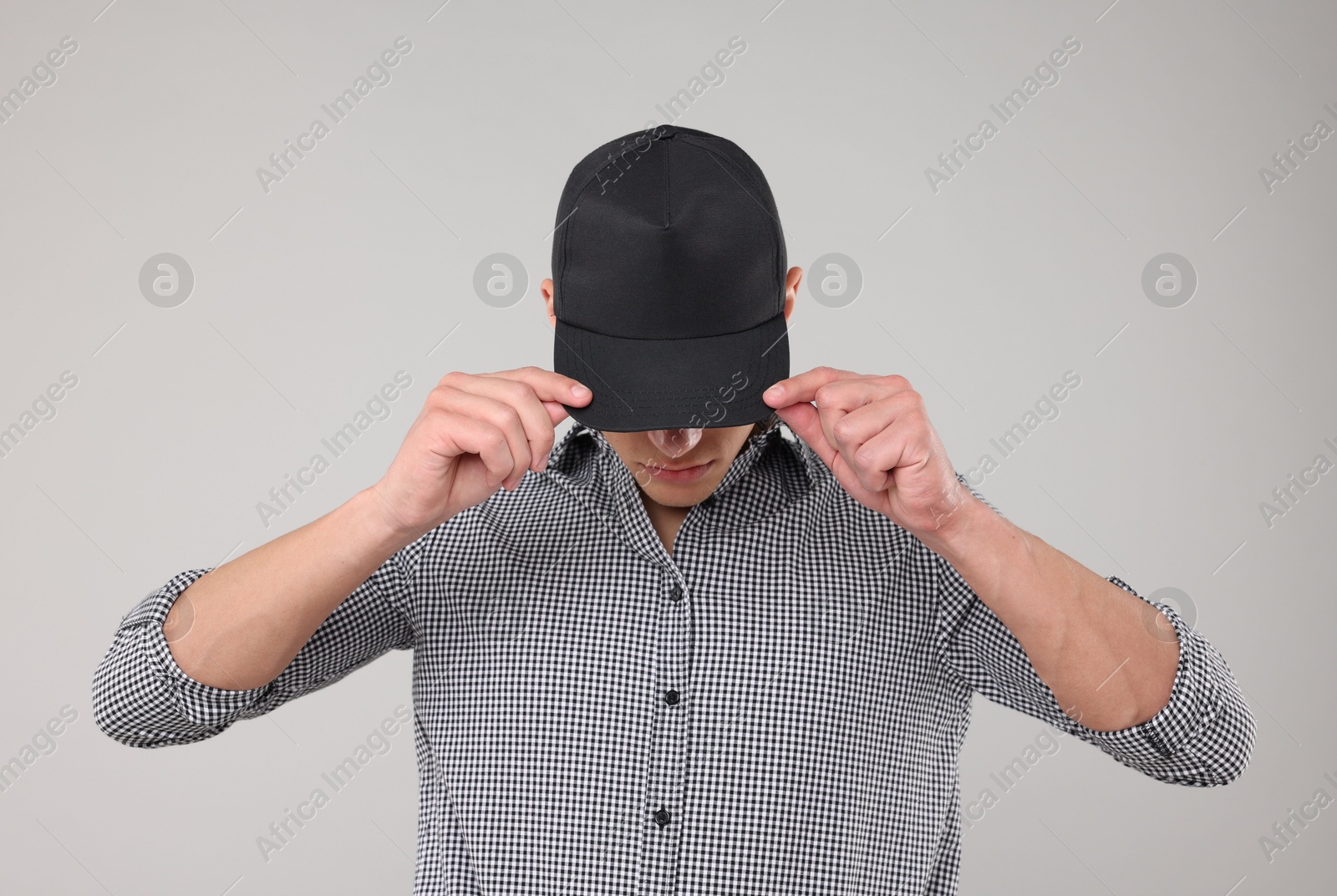 Young man wearing stylish black baseball hat on light grey background Photo of Young man wearing stylish black baseball hat on light grey background