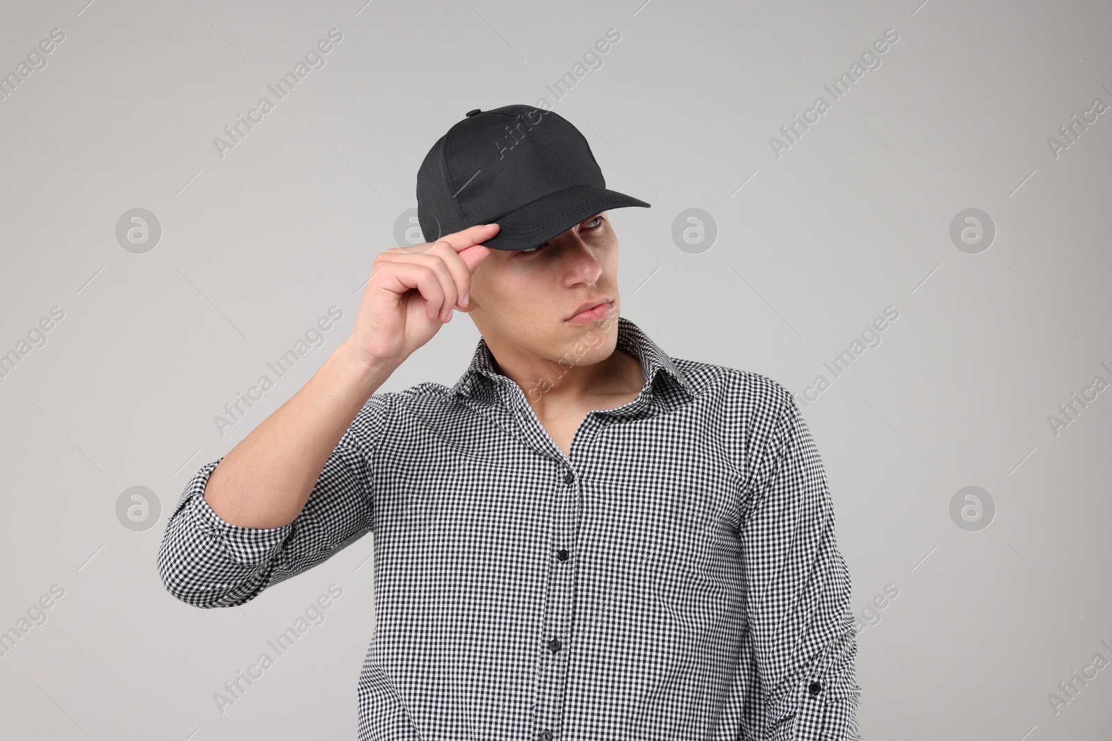 Young man wearing stylish black baseball hat on light grey background Photo of Young man wearing stylish black baseball hat on light grey background