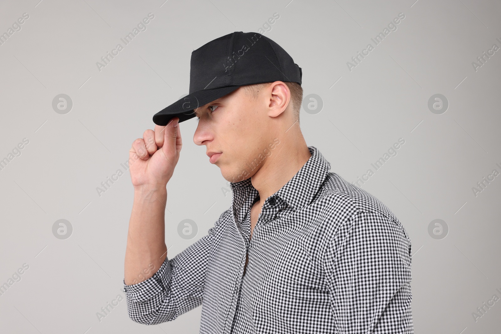 Young man wearing stylish black baseball hat on light grey background Photo of Young man wearing stylish black baseball hat on light grey background