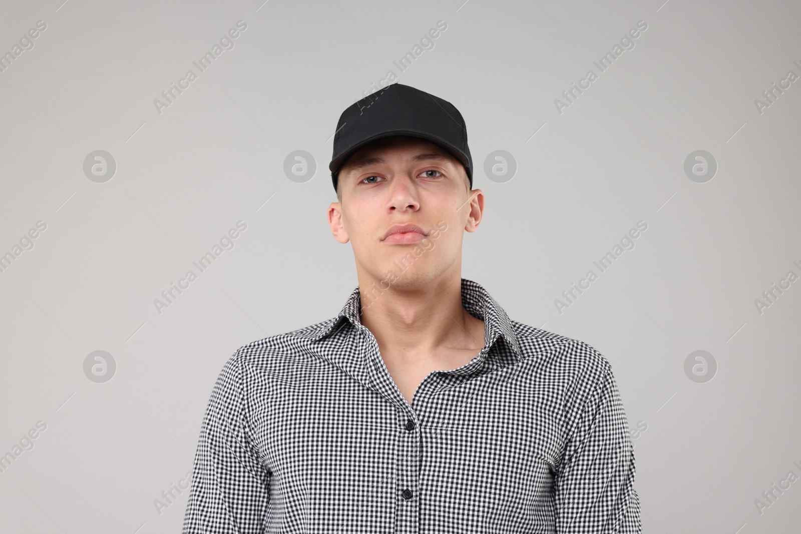 Young man wearing stylish black baseball hat on light grey background Photo of Young man wearing stylish black baseball hat on light grey background