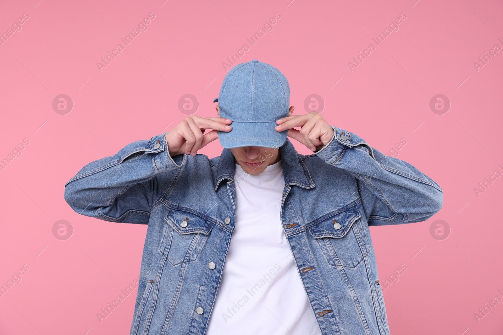 Young man wearing stylish denim baseball hat on pink background Photo of Young man wearing stylish denim baseball hat on pink background