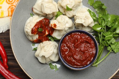 Photo of Tasty khinkali with spices, sauce and cilantro on wooden table, flat lay