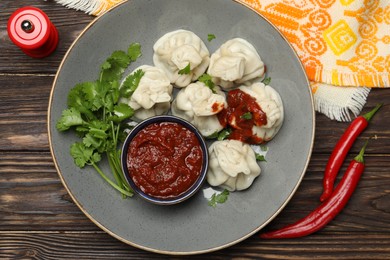 Photo of Tasty khinkali with spices, sauce and cilantro on wooden table, flat lay