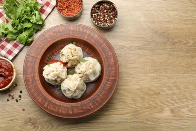 Photo of Tasty khinkali with sauce and spices on wooden table, flat lay. Space for text