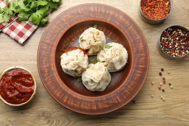Photo of Tasty khinkali with sauce and spices on wooden table, flat lay