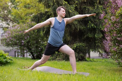 Photo of Young man practicing yoga on mat in park