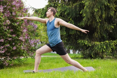 Photo of Young man practicing yoga on mat in park