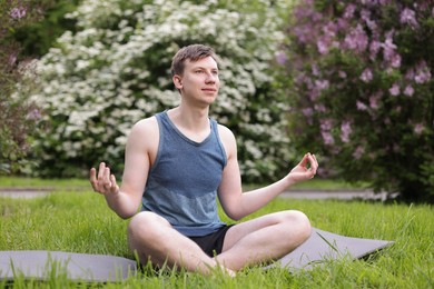 Photo of Young man practicing yoga on mat in park