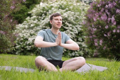 Photo of Young man practicing yoga on mat in park