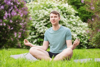 Photo of Young man practicing yoga on mat in park