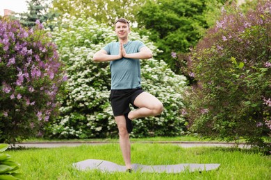 Photo of Young man practicing yoga on mat in park
