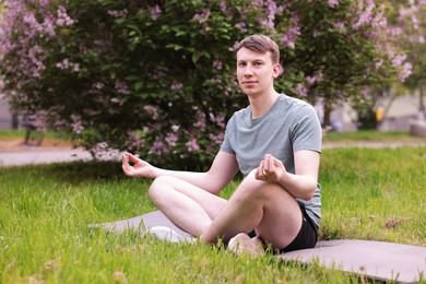 Photo of Young man practicing yoga on mat in park