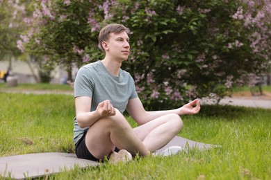 Photo of Young man practicing yoga on mat in park