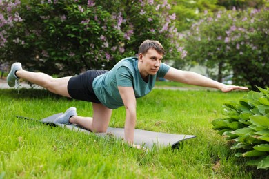 Photo of Young man practicing yoga on mat in park