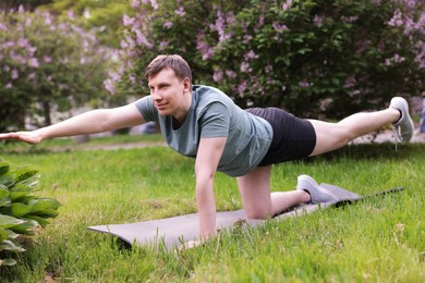 Photo of Young man practicing yoga on mat in park
