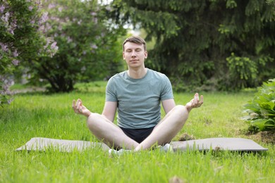Photo of Young man practicing yoga on mat in park
