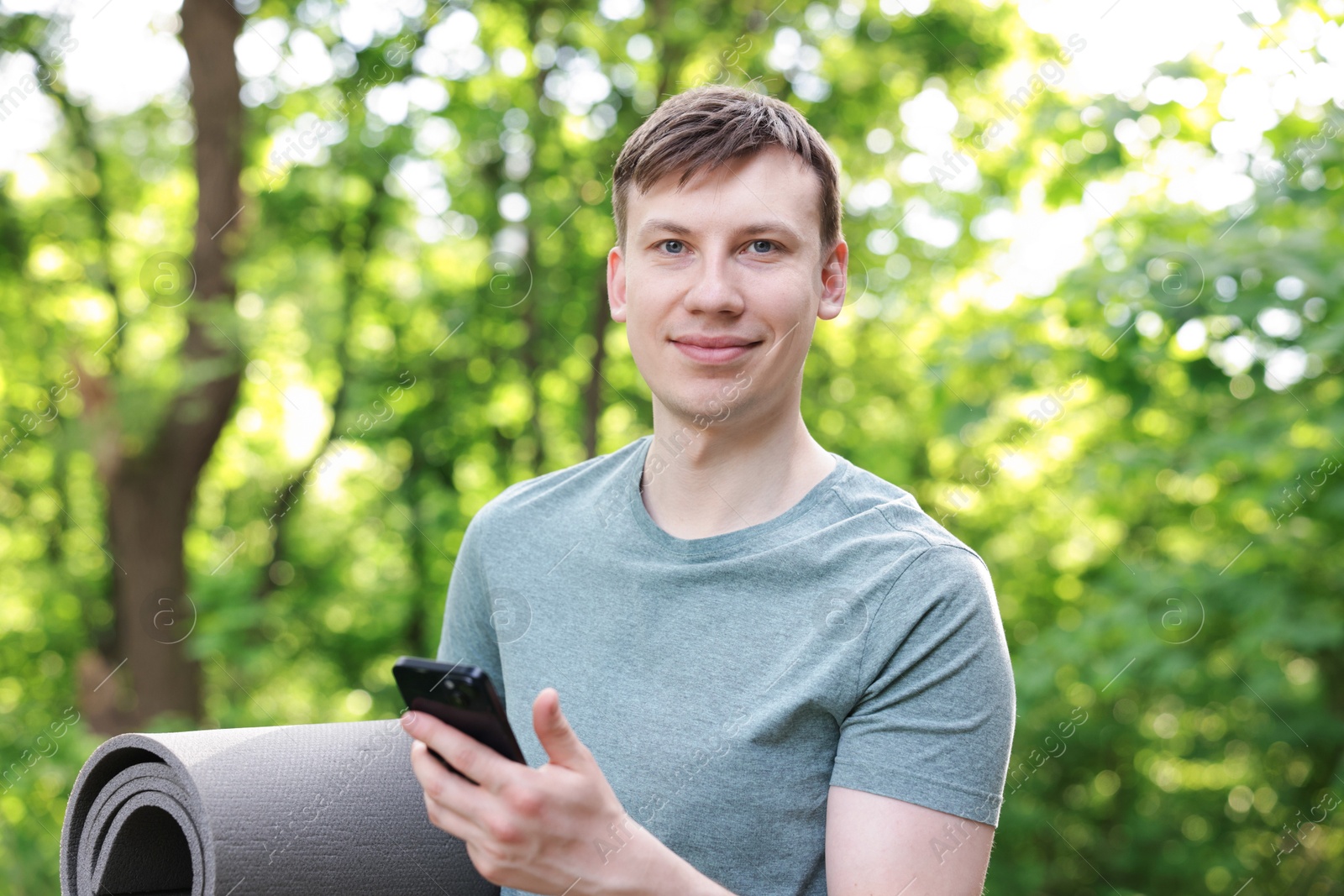 Photo of Young man with yoga mat and phone in park