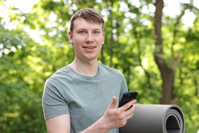 Photo of Young man with yoga mat and phone in park