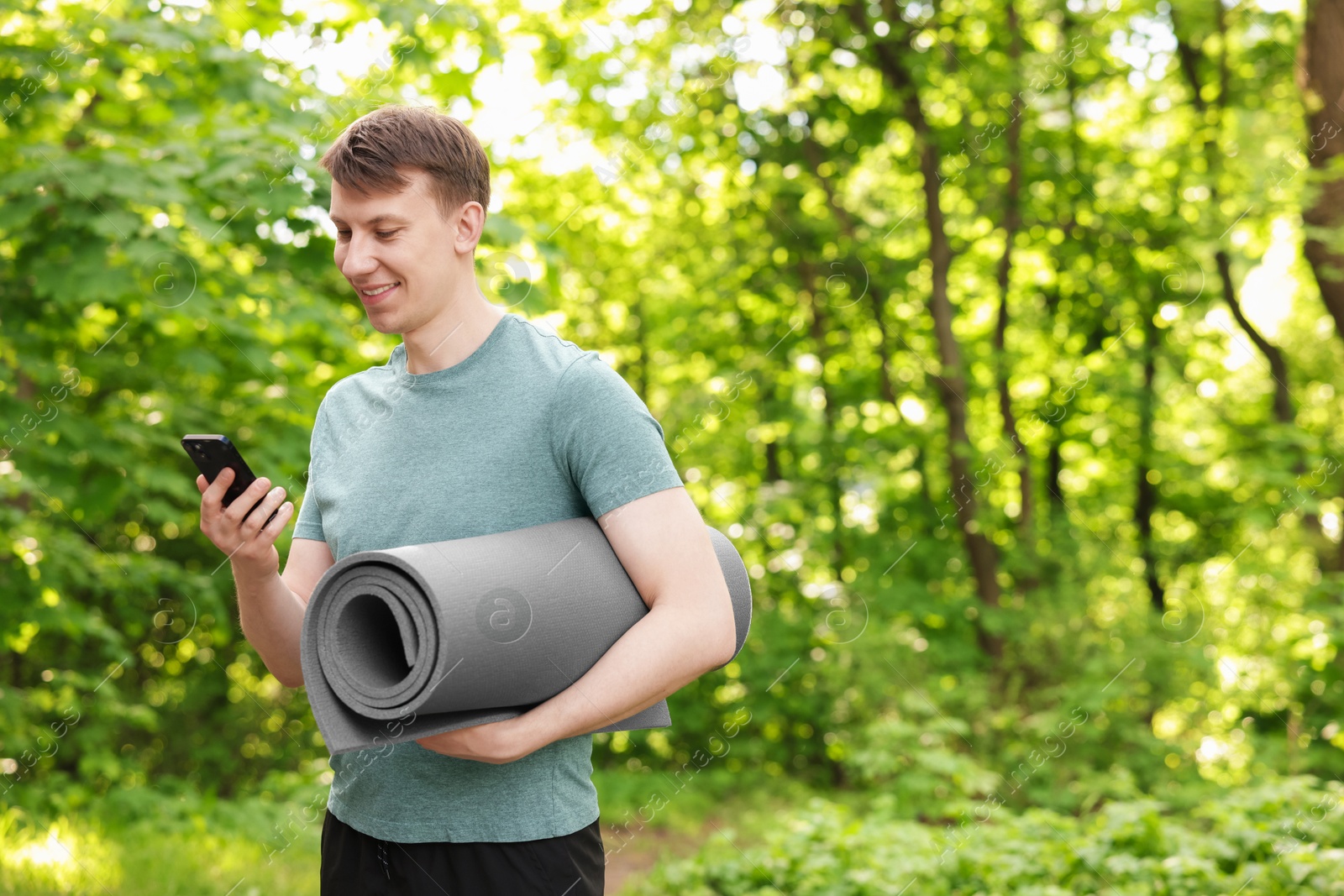 Photo of Young man with yoga mat and phone in park, space for text