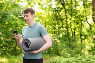 Photo of Young man with yoga mat and phone in park, space for text