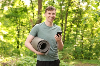 Photo of Young man with yoga mat and phone in park, space for text