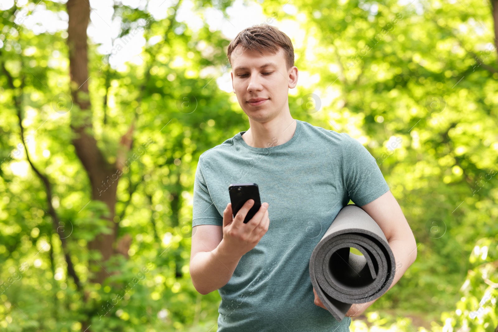 Photo of Young man with yoga mat and phone in park