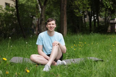 Photo of Young man practicing yoga on mat in park