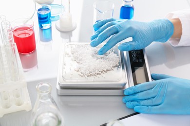 Photo of Scientist weighing sample on scales at white mirror table, closeup