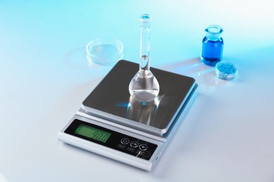 Photo of Scale with samples and laboratory glassware on white table in color lights, closeup