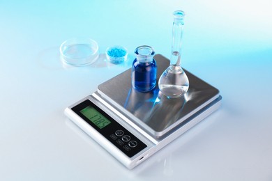 Photo of Scale with samples and laboratory glassware on white table in color lights, closeup