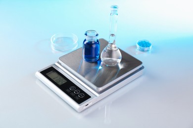 Photo of Scale with samples and laboratory glassware on white table in color lights, closeup
