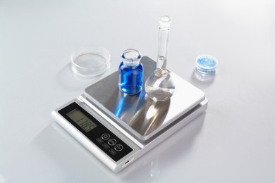Photo of Scale with samples and laboratory glassware on white table in color lights, closeup