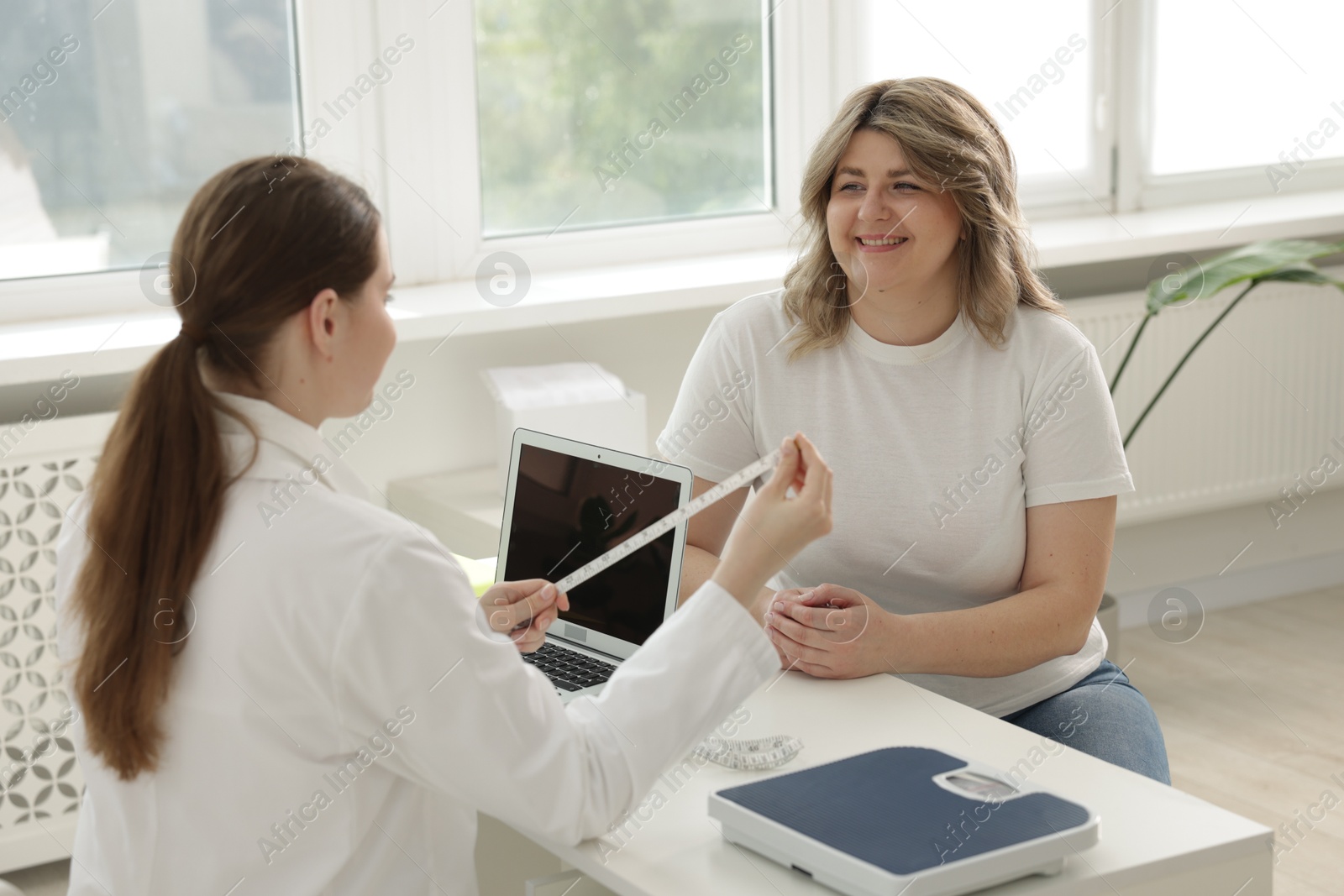 Weight loss. Nutritionist consulting overweight woman at white desk in clinic Photo of Weight loss. Nutritionist consulting overweight woman at white desk in clinic
