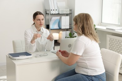 Photo of Weight loss. Nutritionist consulting overweight woman at white desk in clinic