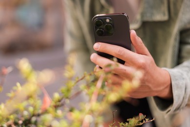 Photo of Man using plant recognition application on smartphone outdoors, closeup. Space for text