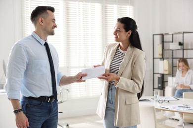 Photo of Money bonus. Boss giving envelope to employee in office