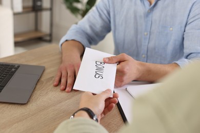 Photo of Boss giving envelope with word bonus to employee in office, closeup