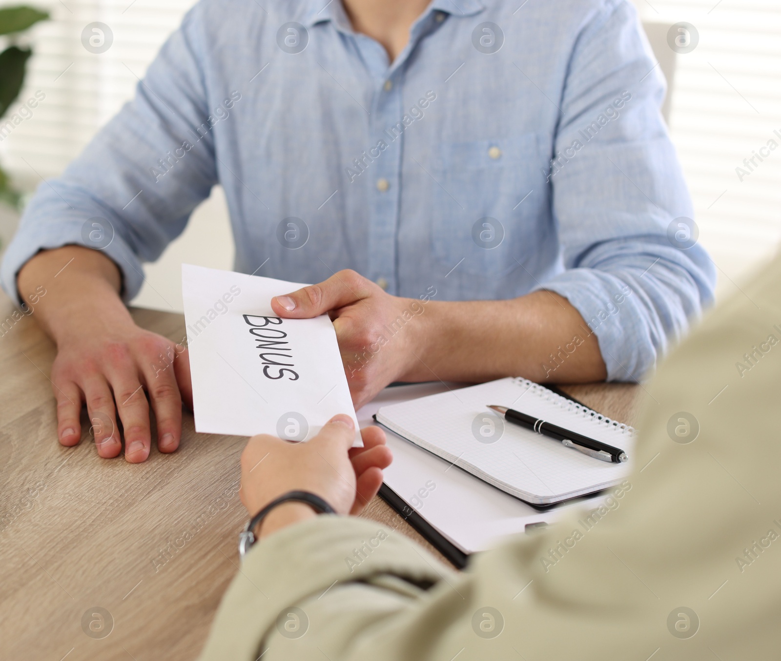 Boss giving envelope with word bonus to employee in office, closeup Photo of Boss giving envelope with word bonus to employee in office, closeup
