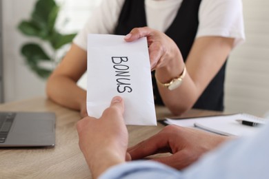 Photo of Boss giving envelope with word bonus to employee in office, closeup