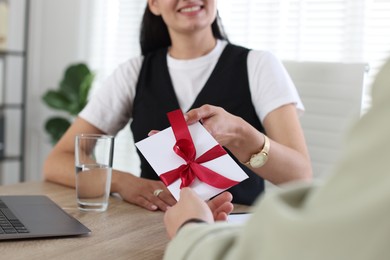 Photo of Money bonus. Boss giving envelope with bow to employee in office, closeup