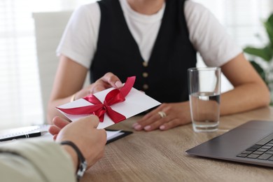 Photo of Money bonus. Boss giving envelope with bow to employee in office, closeup