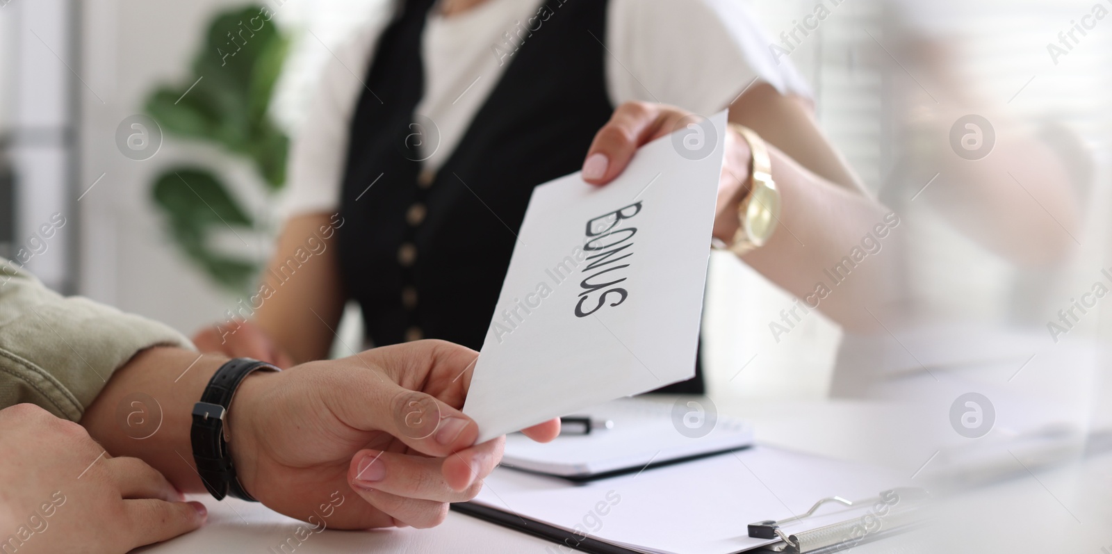 Boss giving envelope with word bonus to employee in office, closeup Photo of Boss giving envelope with word bonus to employee in office, closeup