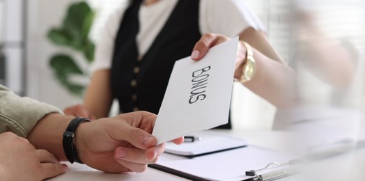 Photo of Boss giving envelope with word bonus to employee in office, closeup