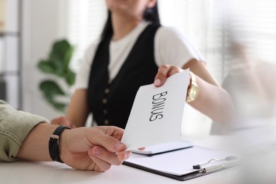 Photo of Boss giving envelope with word bonus to employee in office, closeup