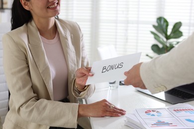 Photo of Employee receiving envelope with word Bonus from boss in office, closeup