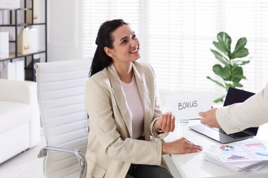 Photo of Employee receiving envelope with word Bonus from boss in office